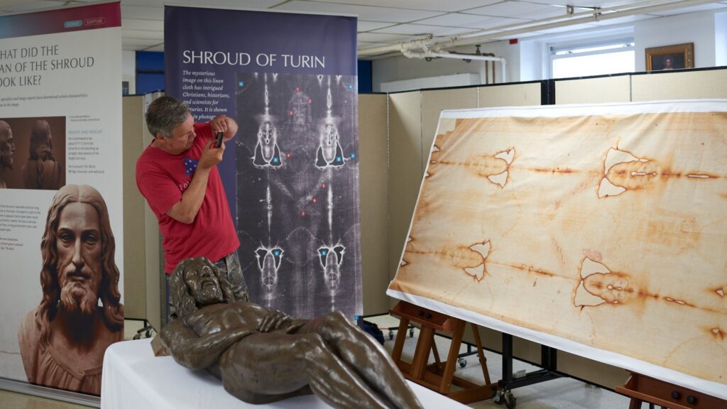 Visitor photographing the full-length Shroud replica beside the bronze sculpture